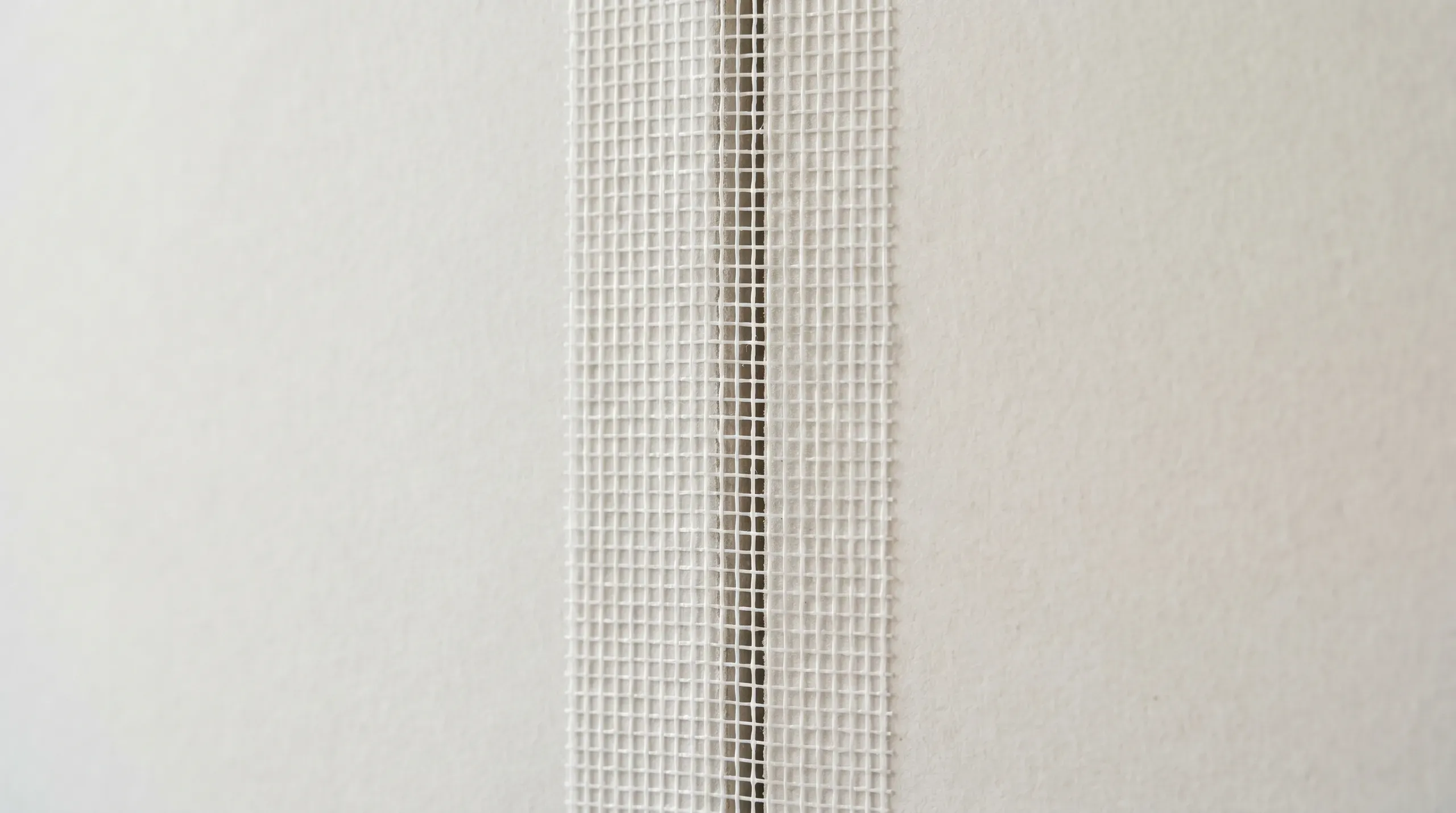 Close-up of self-adhesive fibreglass mesh scrim tape applied centrally over the joint between two sheets of plasterboard, ready for skim coat