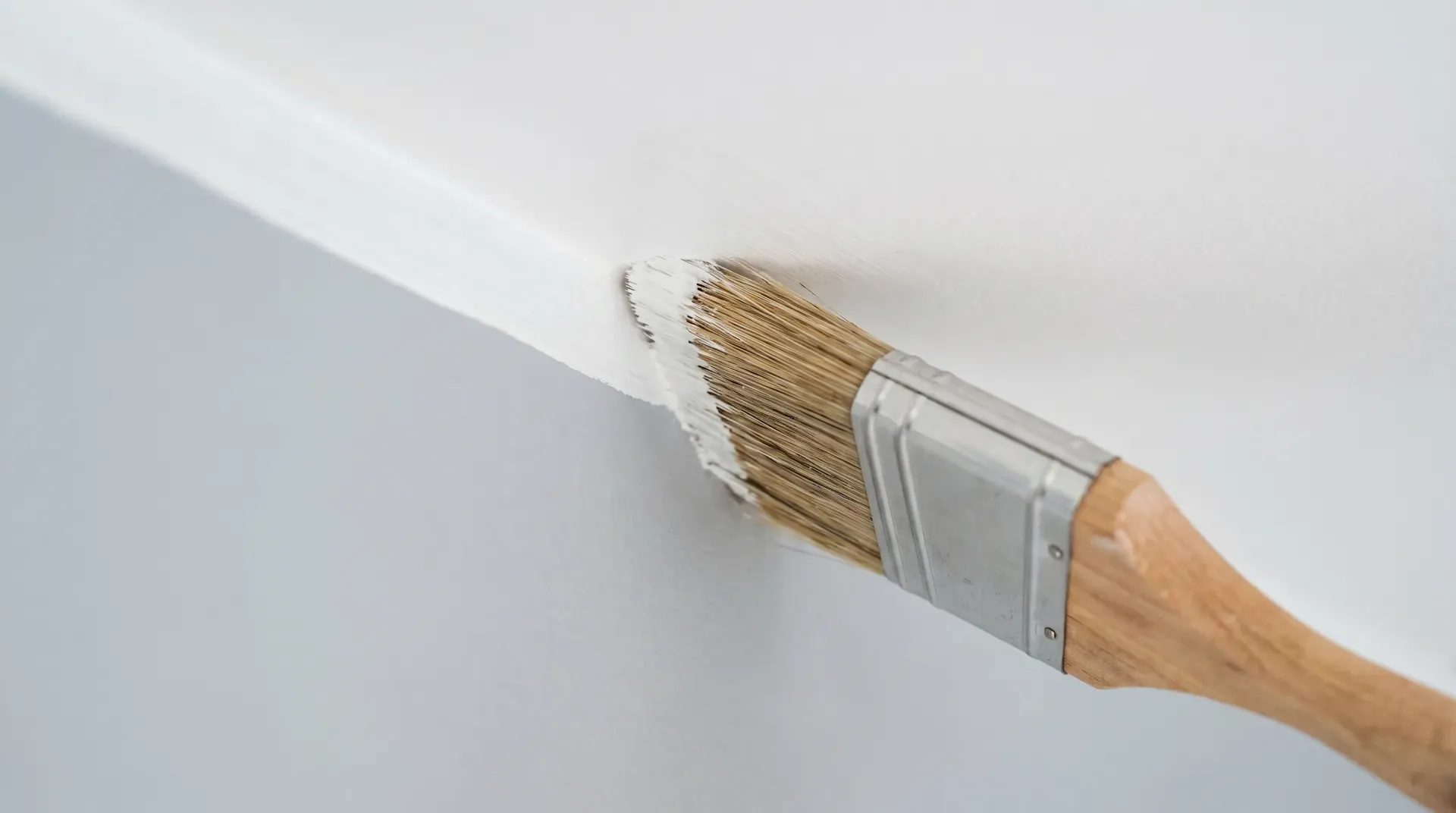 Close-up of a 2-inch angled brush running a clean line of paint along the junction between a wall and ceiling.