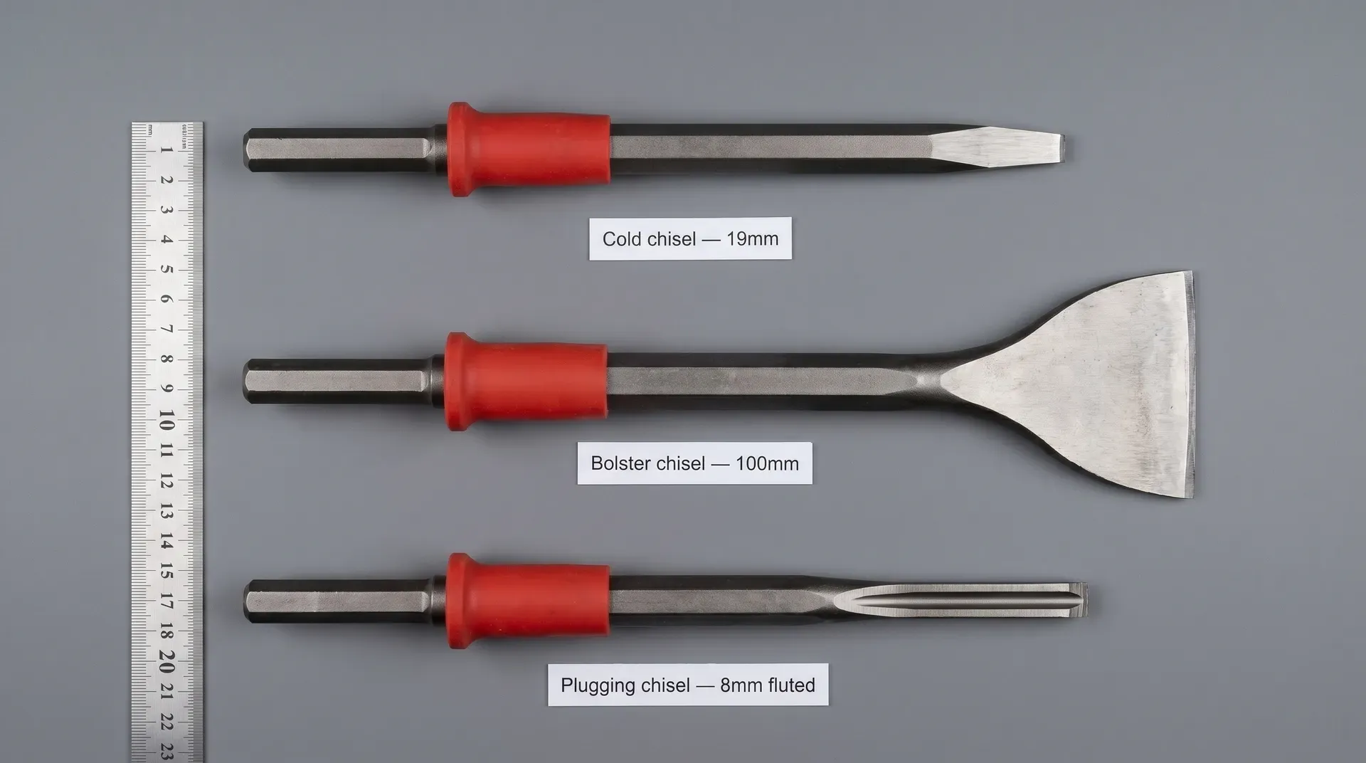 Three masonry chisels laid side by side on a grey surface for scale comparison: a narrow cold chisel at top, a wide bolster chisel in the middle, and a narrow fluted plugging chisel at the bottom, each with a card label showing its blade width