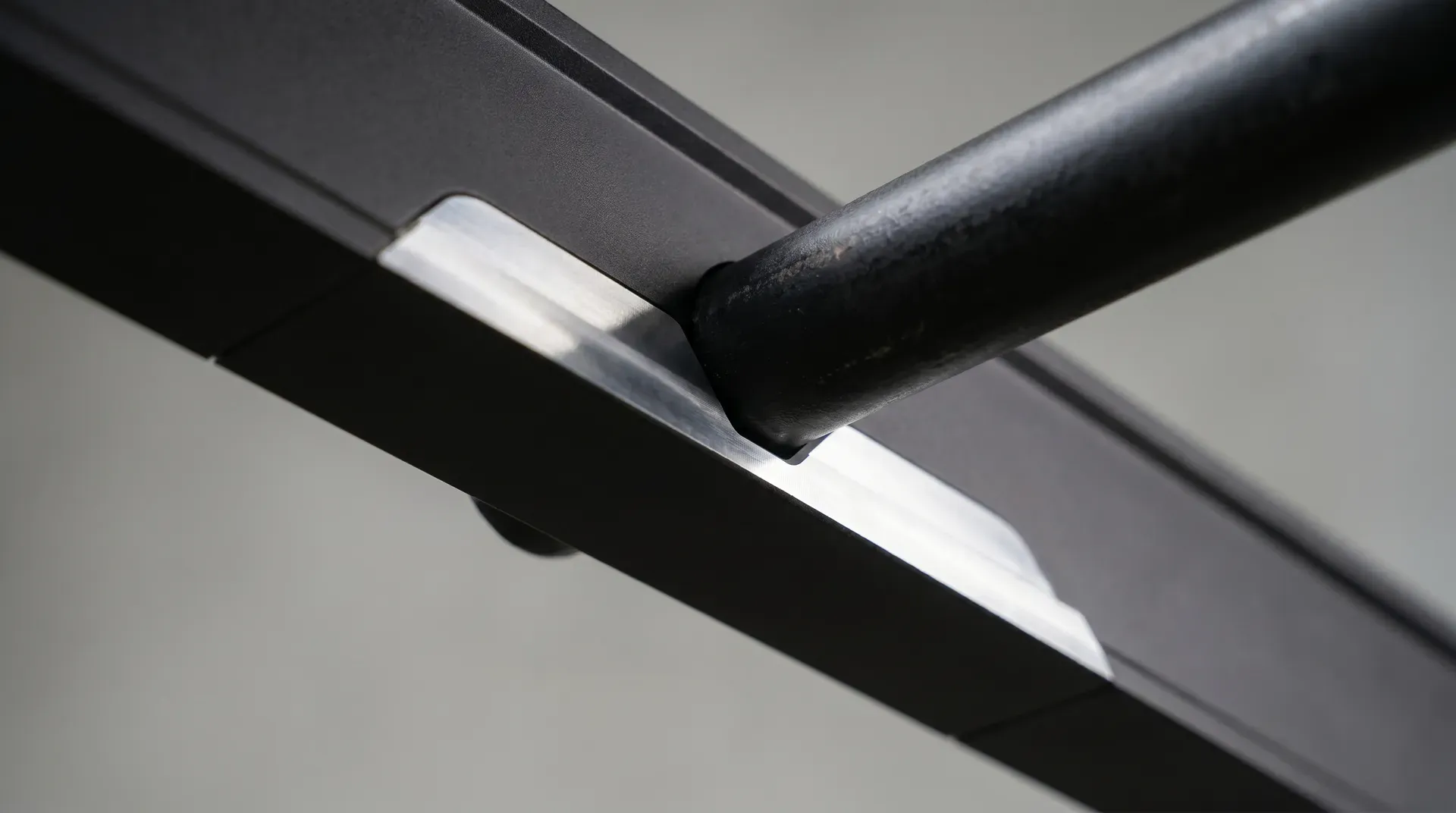 Close-up of the V-groove channel machined into the magnetic base of a spirit level, resting on a 22mm black steel gas pipe with the groove aligned along the pipe's long axis and the magnet gripping hands-free.