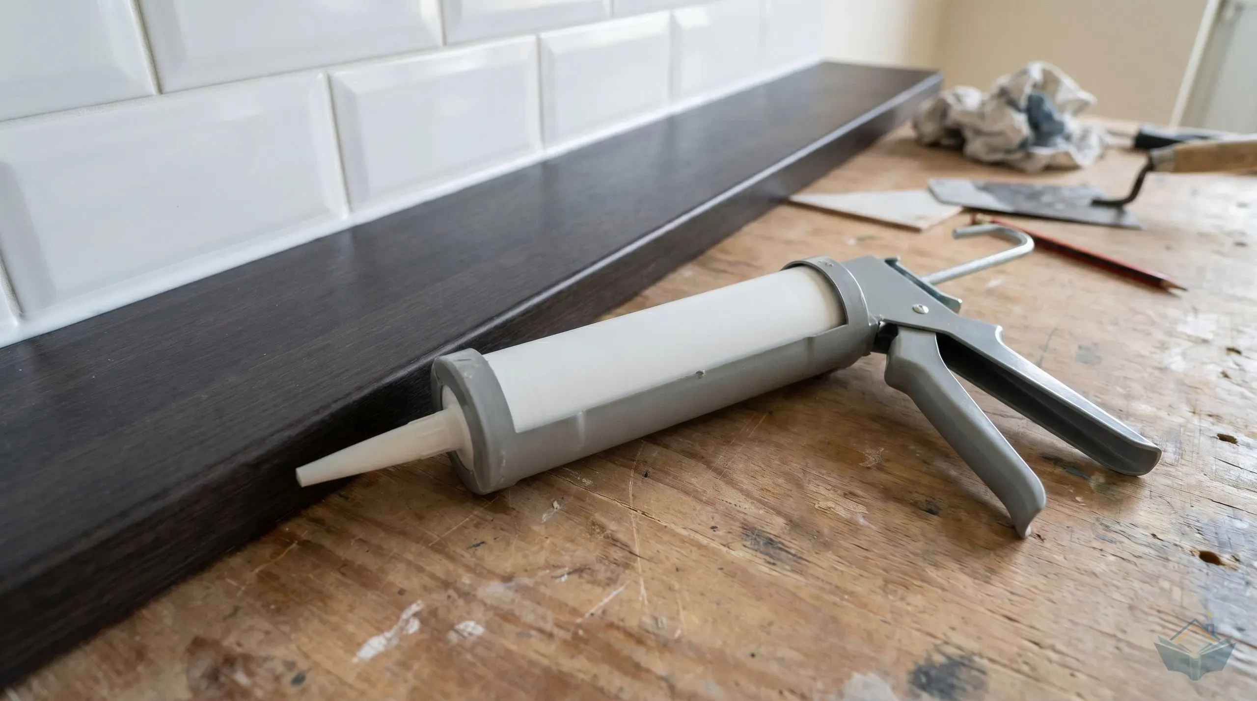 A smooth-rod sealant gun loaded with a 310ml silicone cartridge alongside a kitchen worktop edge with a freshly tooled silicone bead between worktop and tiled splashback