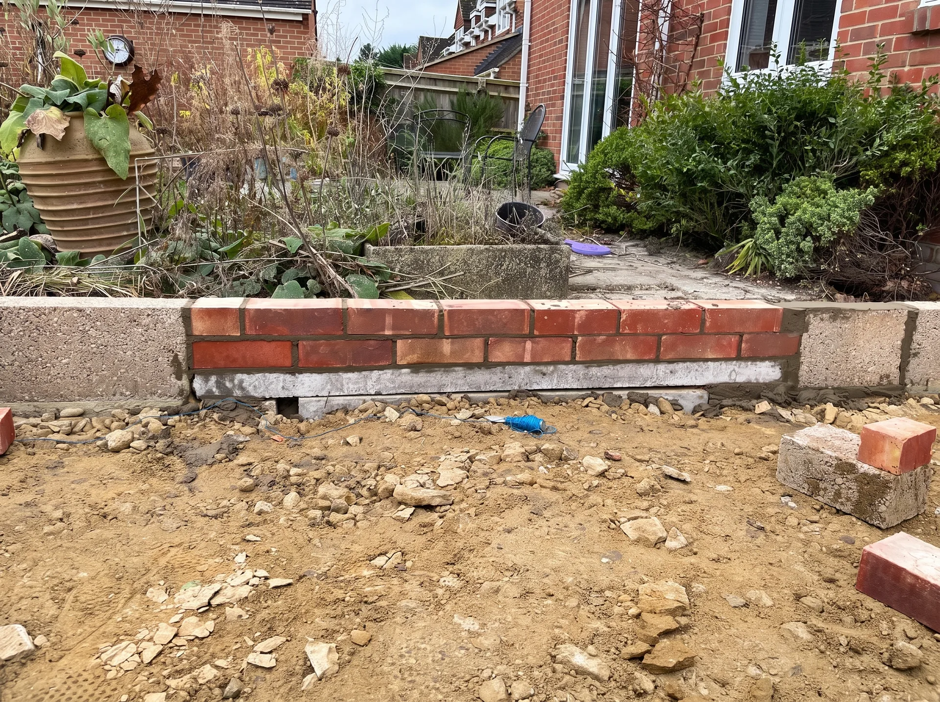 A concrete lintel bridging an opening in low blockwork above a drain run, with courses of brick built over the top and a string line set out along the wall.