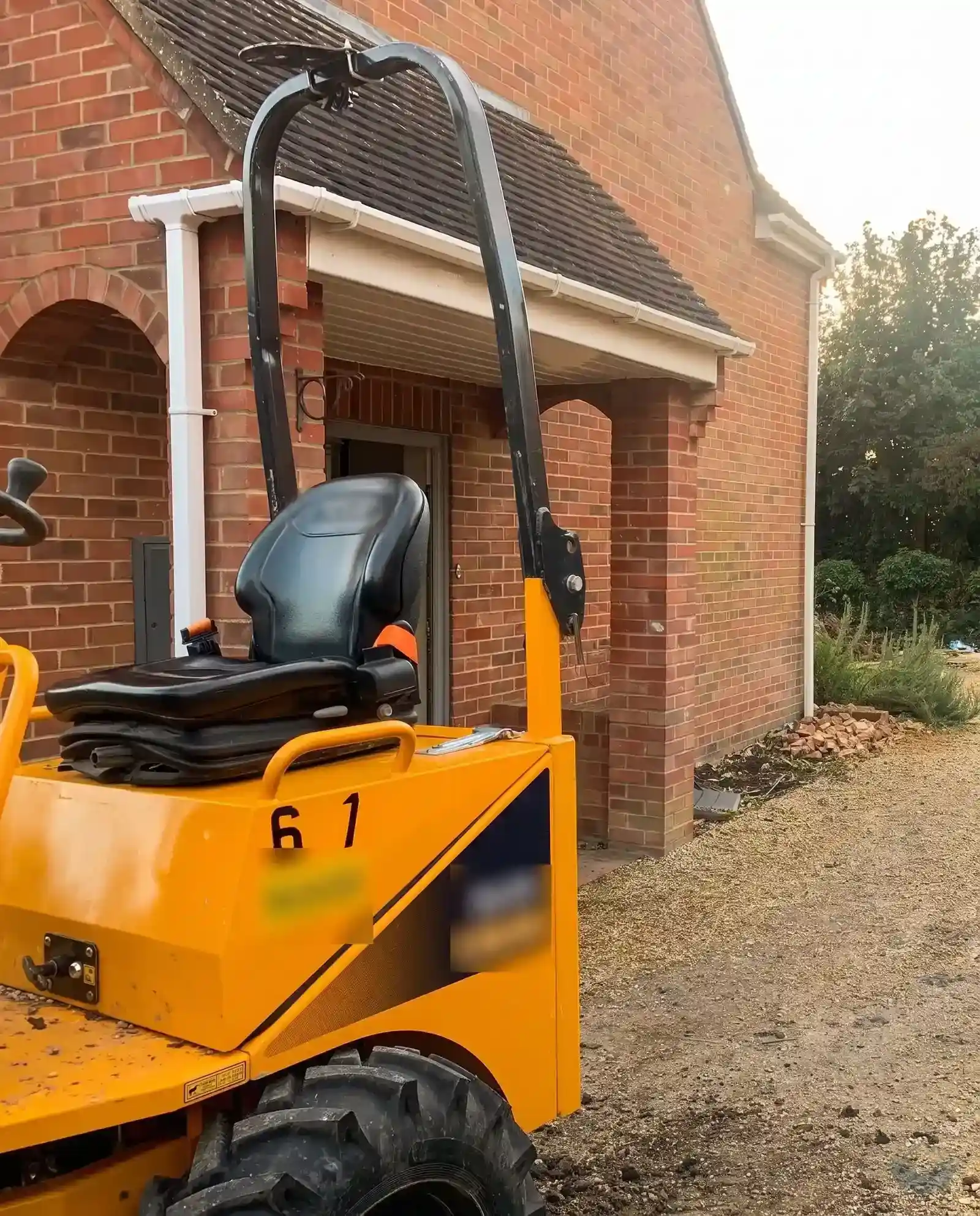 A domestic side garden set up as a building site, with a one tonne tracked digger parked beside the house wall and the marked out extension area in front of it.