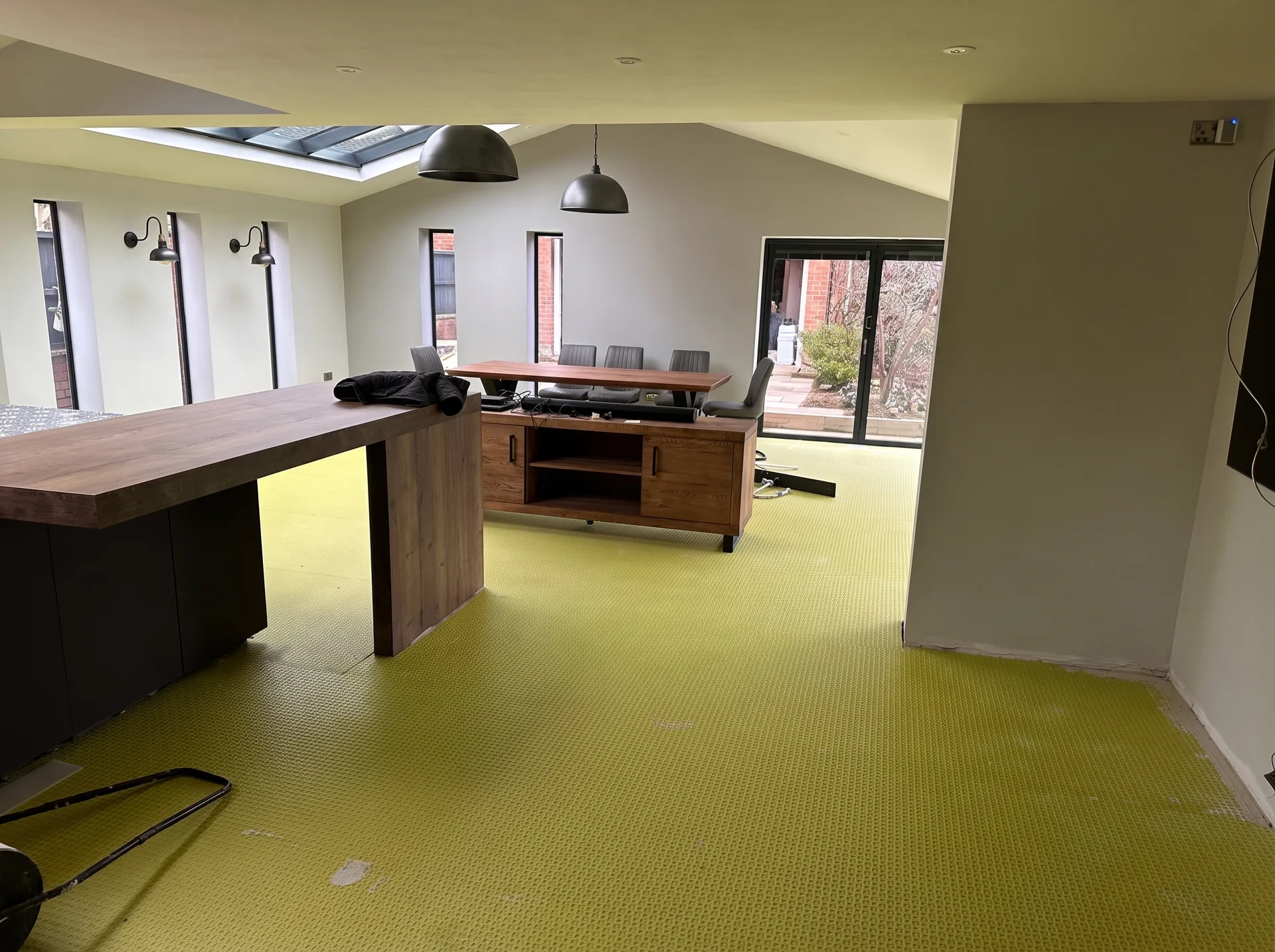 Open-plan kitchen and dining room with a bright green floor preparation layer applied across the whole floor, island and dining furniture in place under a large skylight