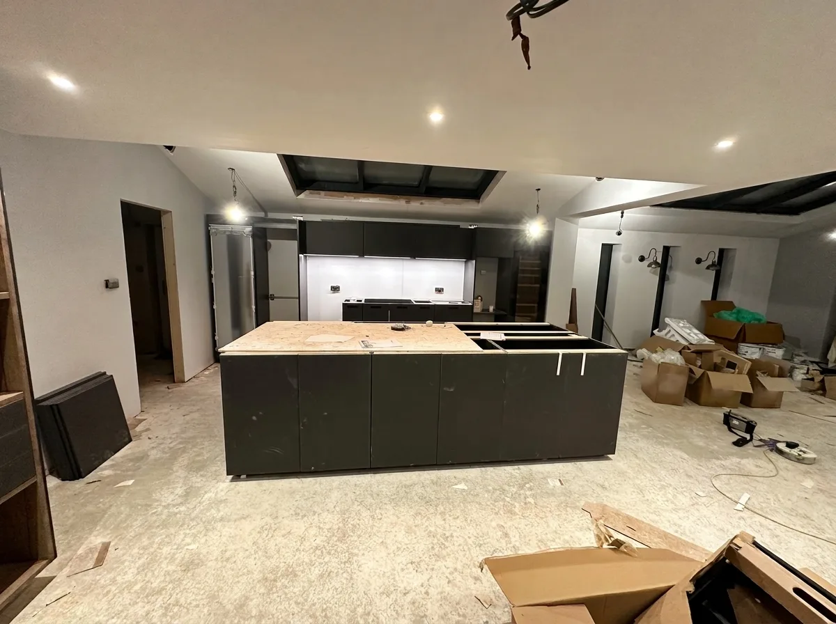 Main run of dark kitchen cabinetry with wall units installed above and tall carcasses housing an integrated fridge freezer at one end and a wine fridge at the other
