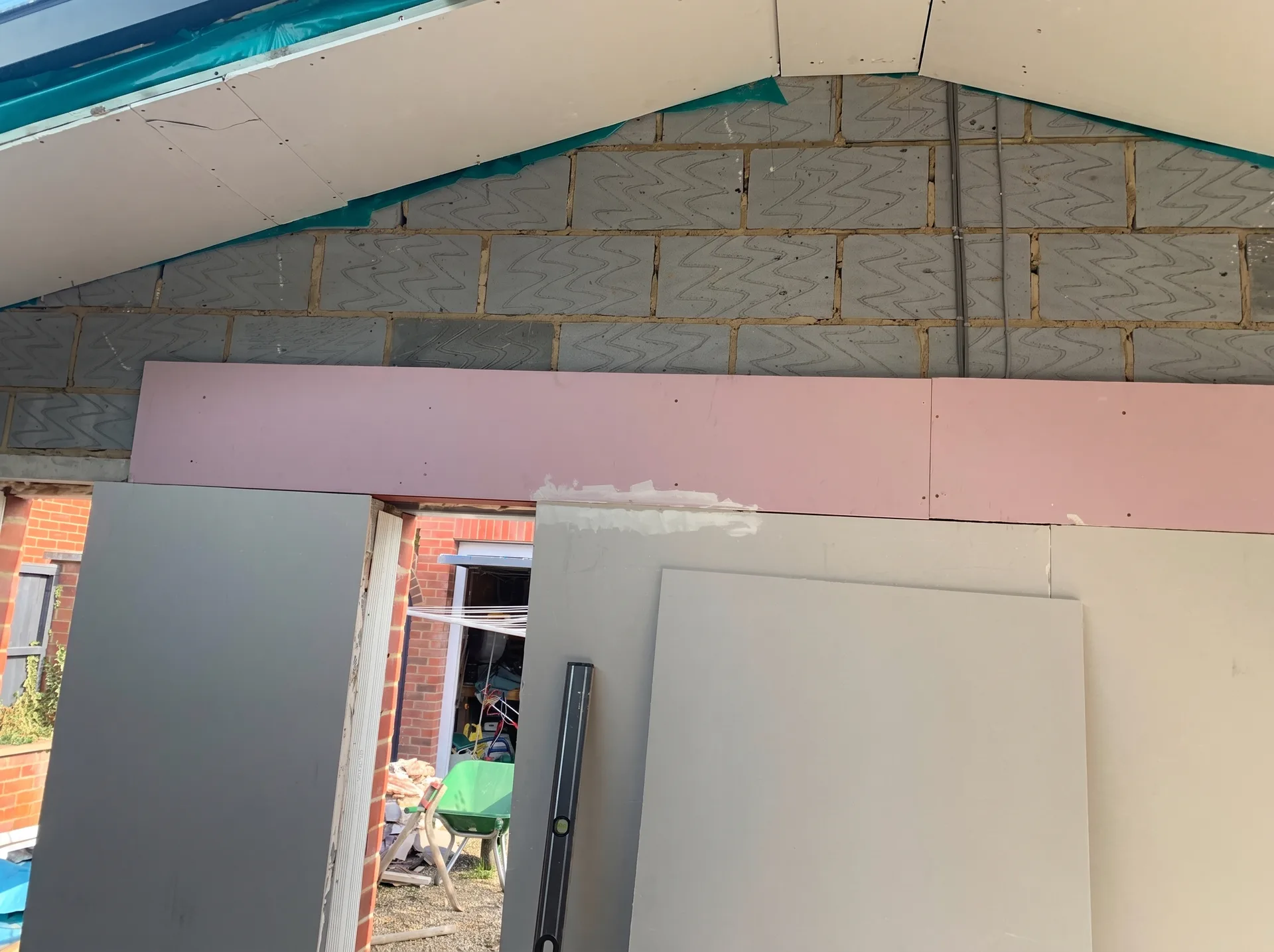 Angled plasterboard ceiling partly installed with green vapour barrier behind, and pink fire-rated board fixed to a blockwork wall beside a steel