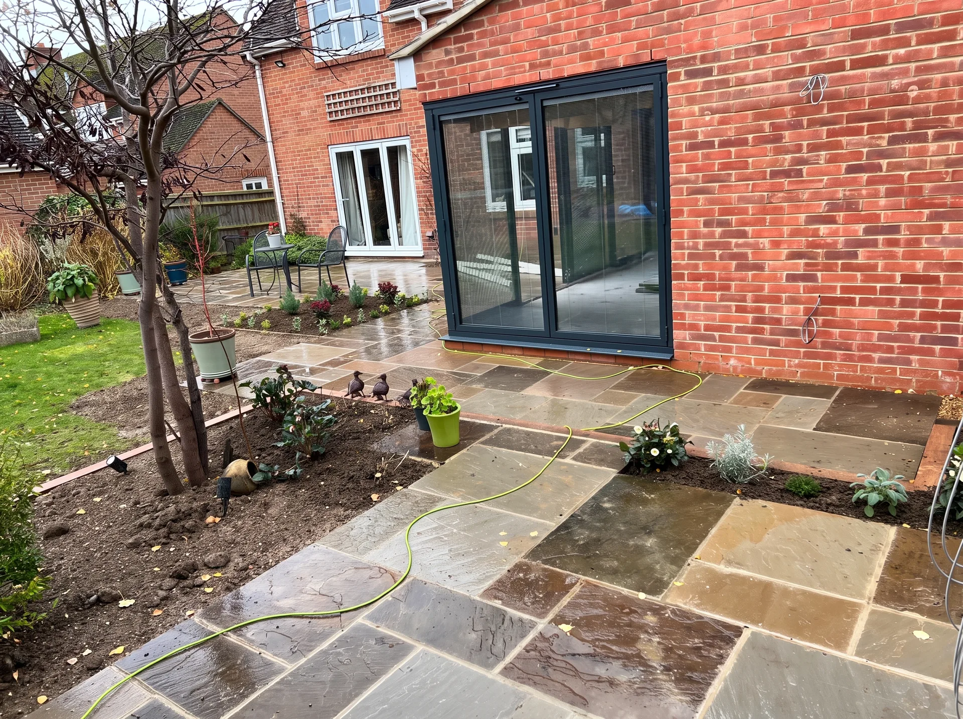 Rear elevation of a finished brick extension with glazed bifold doors, a completed patio in front and new planting in the beds alongside.