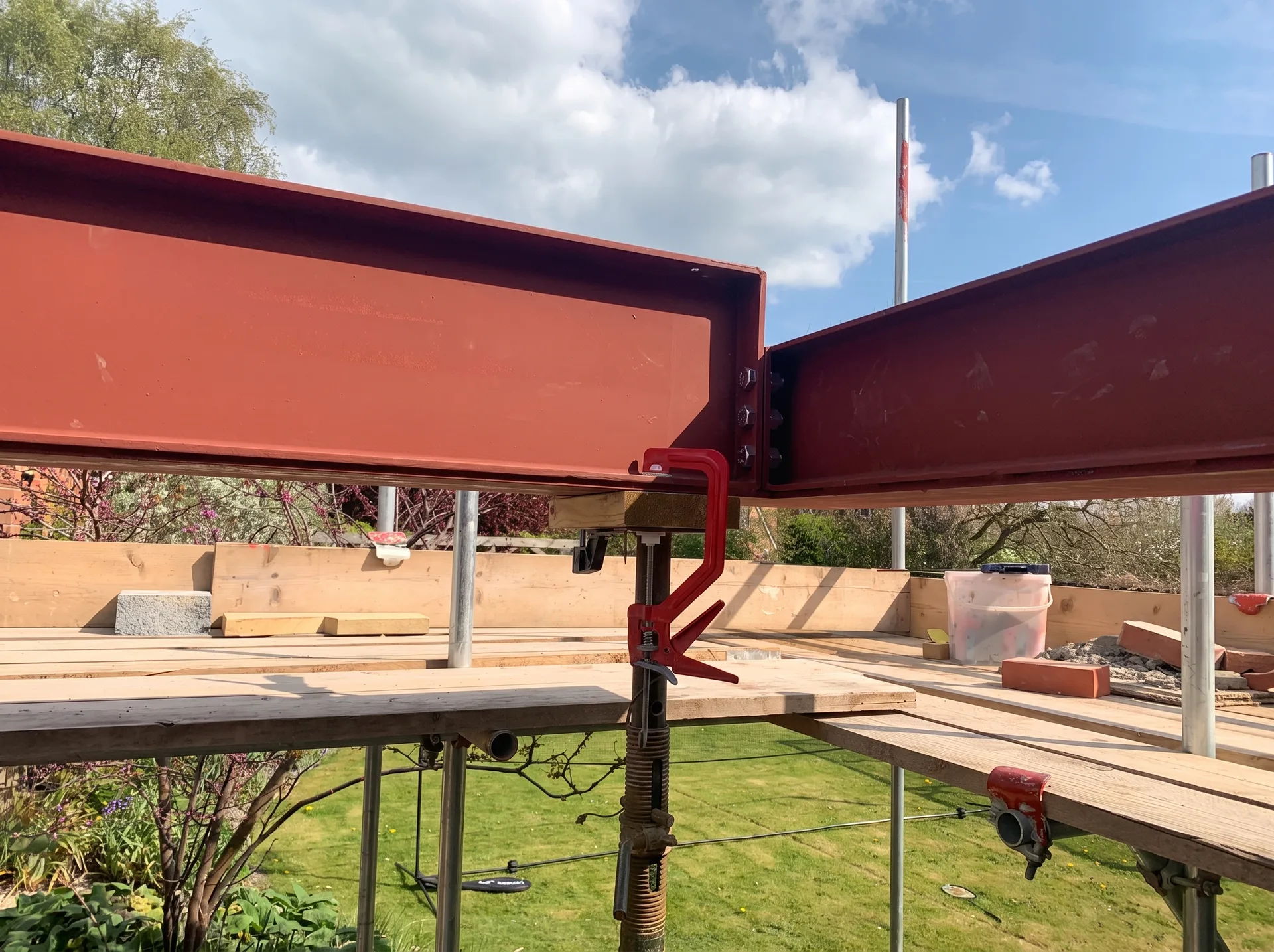 Close view of two painted steel beams meeting at a bolted junction, three large bolts stepping down from the deeper beam to the shallower one.