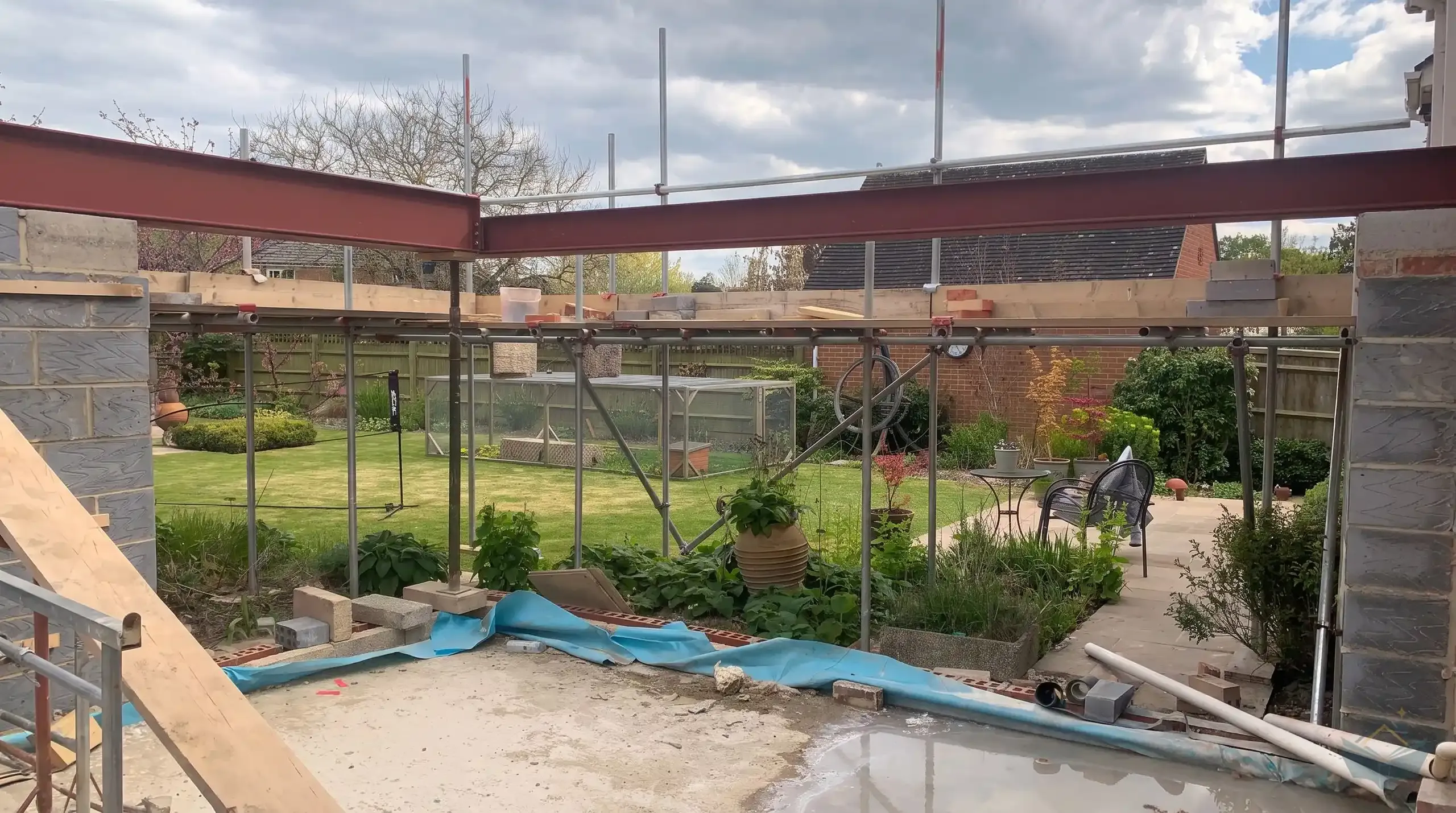 Cantilever steel arrangement at the glazed corner of a rear extension, painted beams carried on a temporary post and scaffolding above new blockwork.