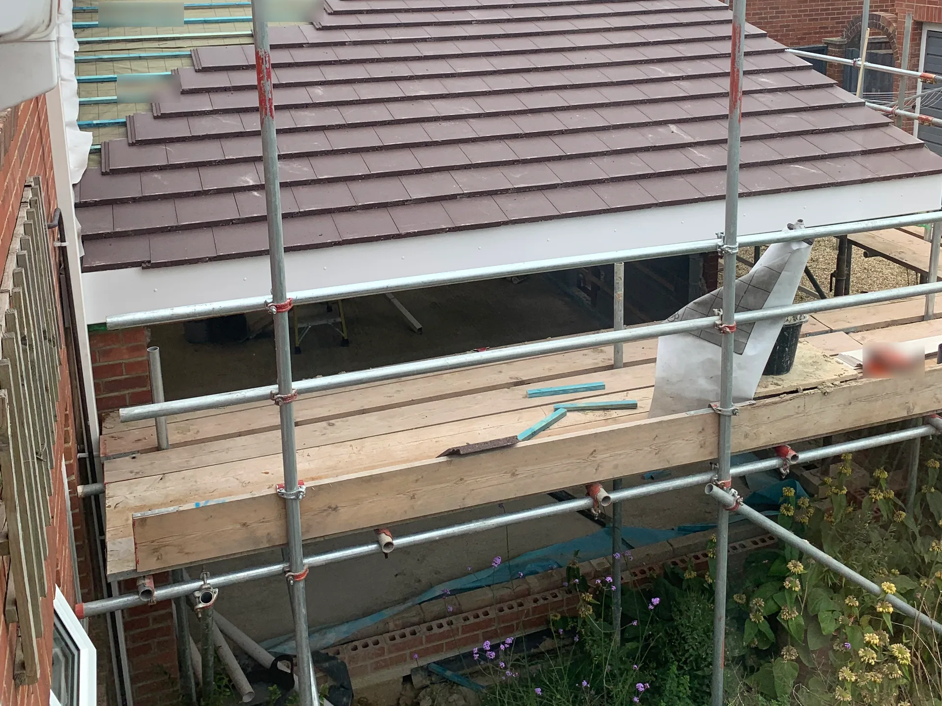 A pitched roof largely covered in clay tiles, with an adjacent section still showing underlay and timber battens.